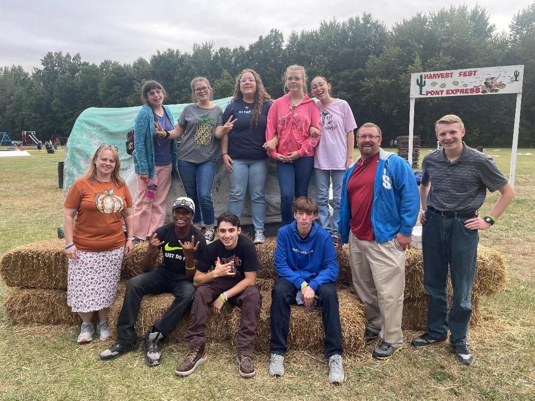 A group of people standing next to hay bales in a field.