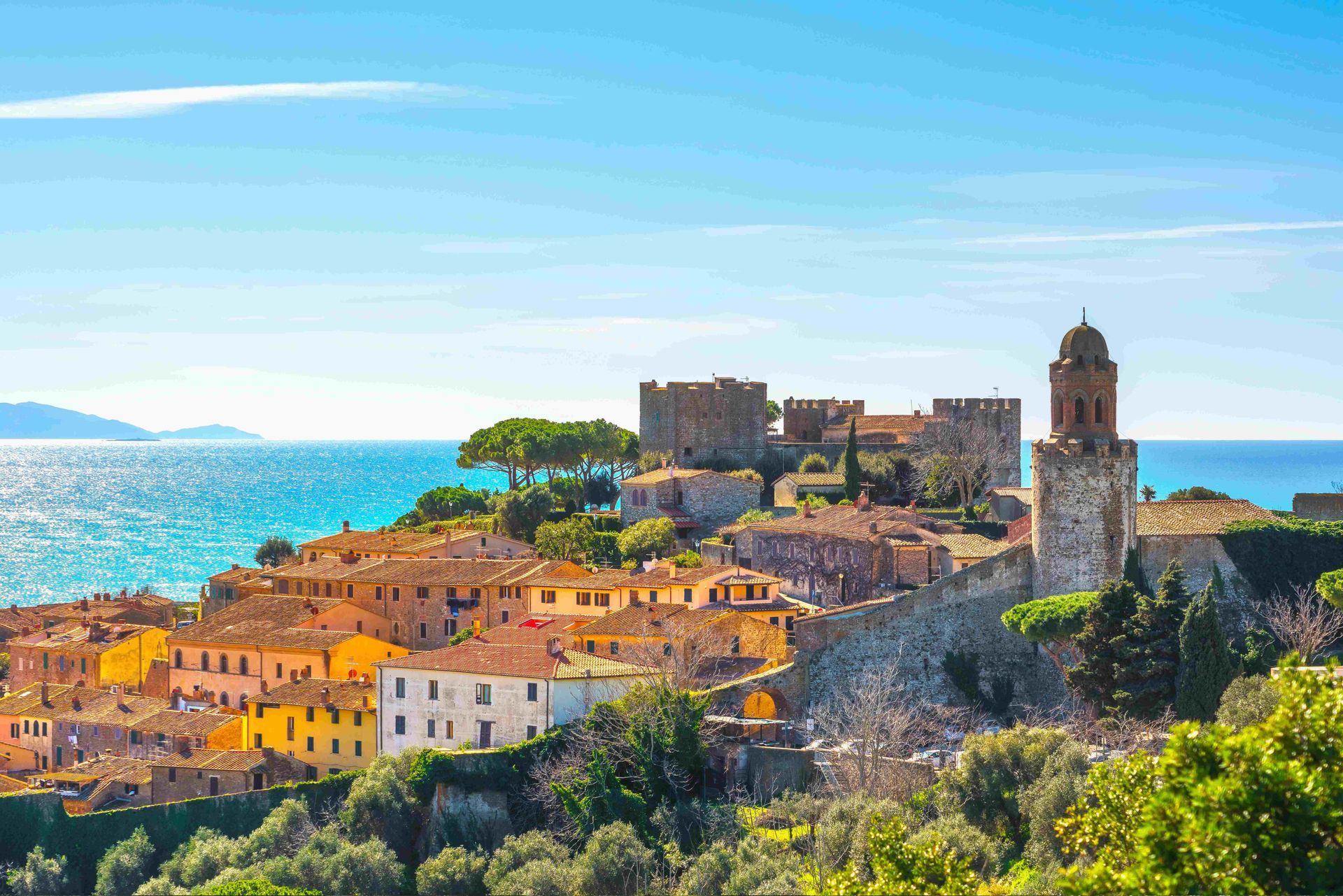 a small town on a hill overlooking the ocean with a castle in the background