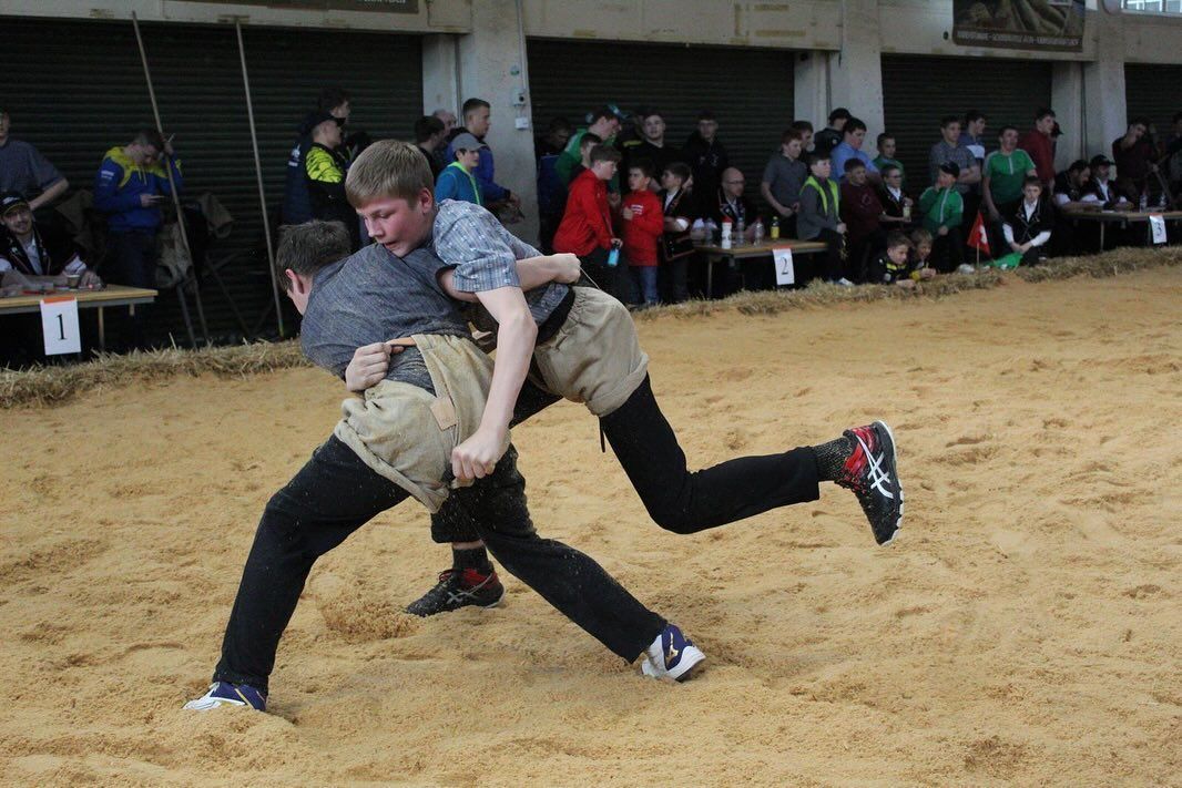 Zwei Jungschwinger Schwingen in einem Sägemehlring, im Hintergrund sind Zuschauer zu sehen.