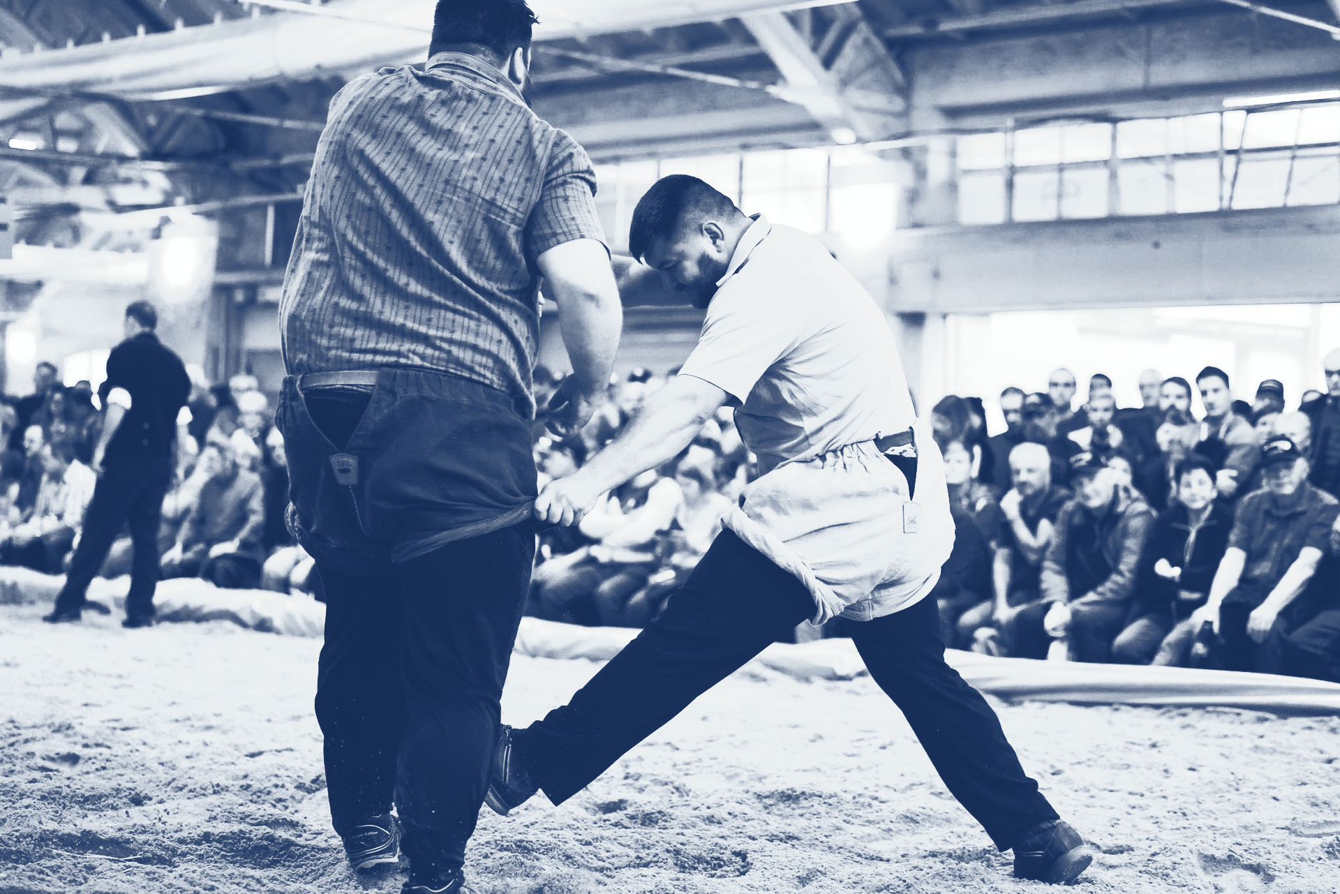 Zwei Männer Schwingen in einer Arena, während ein Publikum zuschaut.