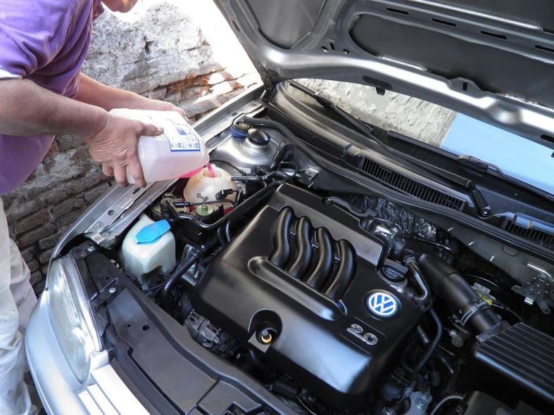 Una persona revisa los fluidos en el compartimento del motor de un Volkswagen con el capó abierto.