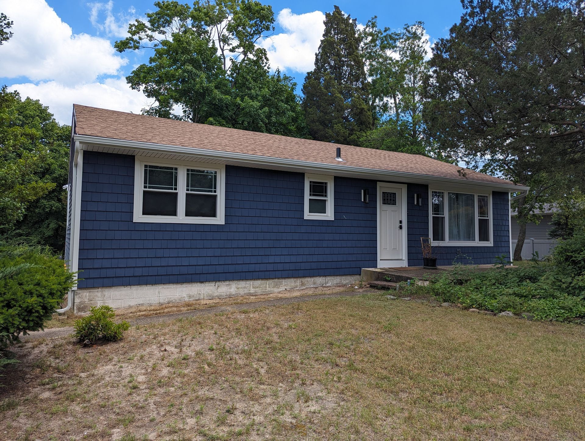 A blue house with a brown roof and white trim is sitting on top of a grassy hill.