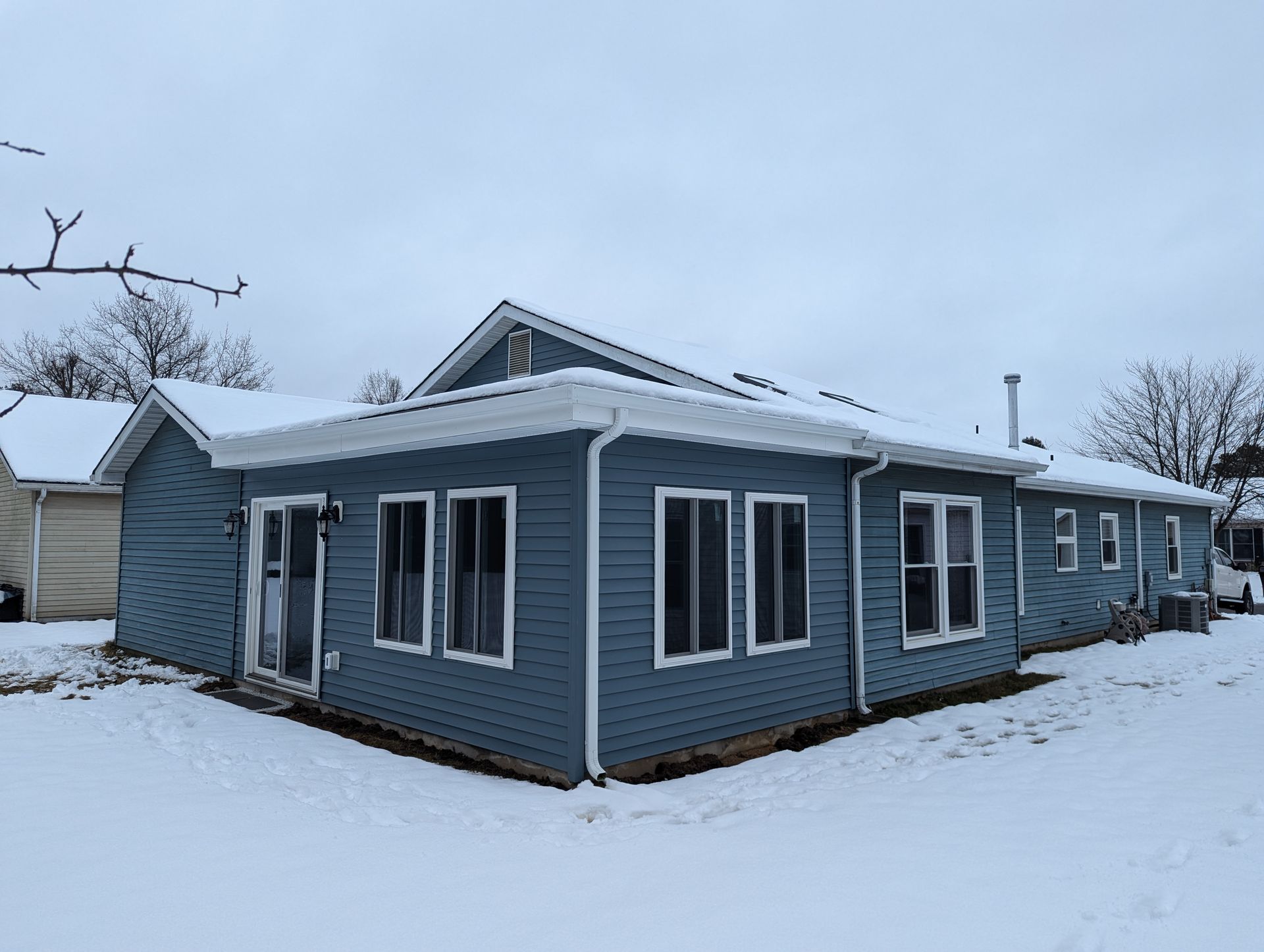 A blue house with a lot of windows is covered in snow.