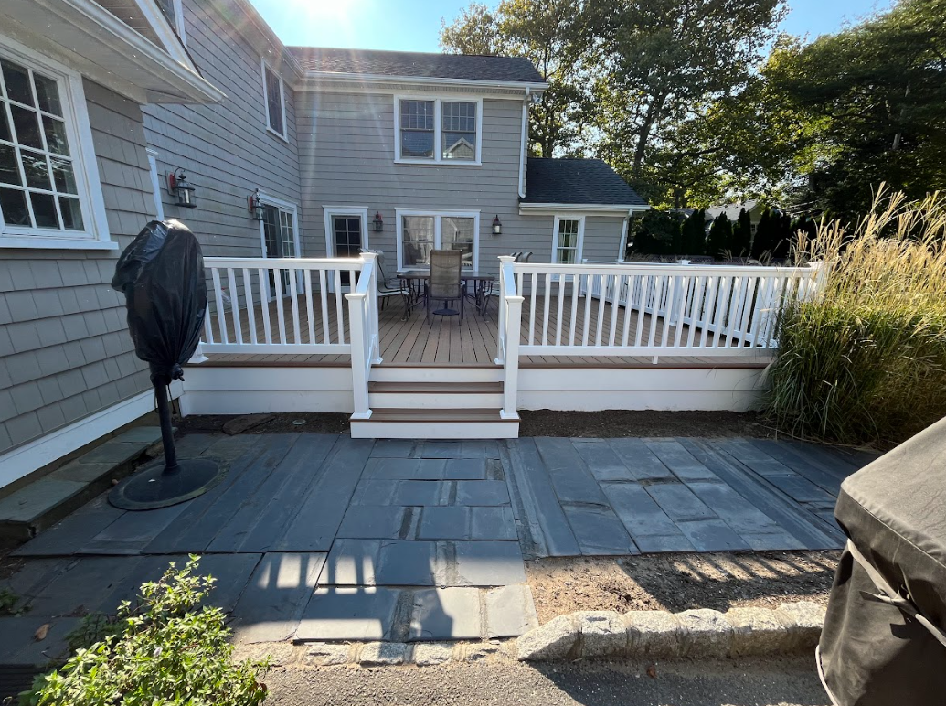 A large deck with a white railing and stairs in front of a house.