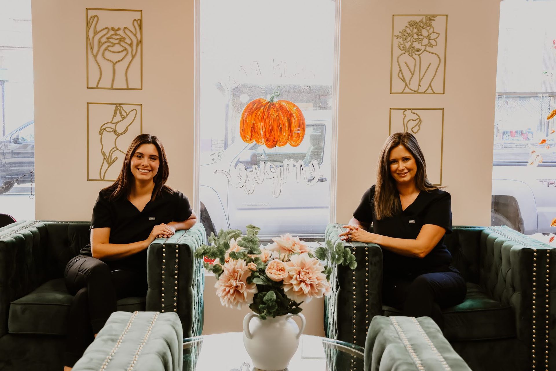 Two women are sitting in chairs in a room with a vase of flowers.