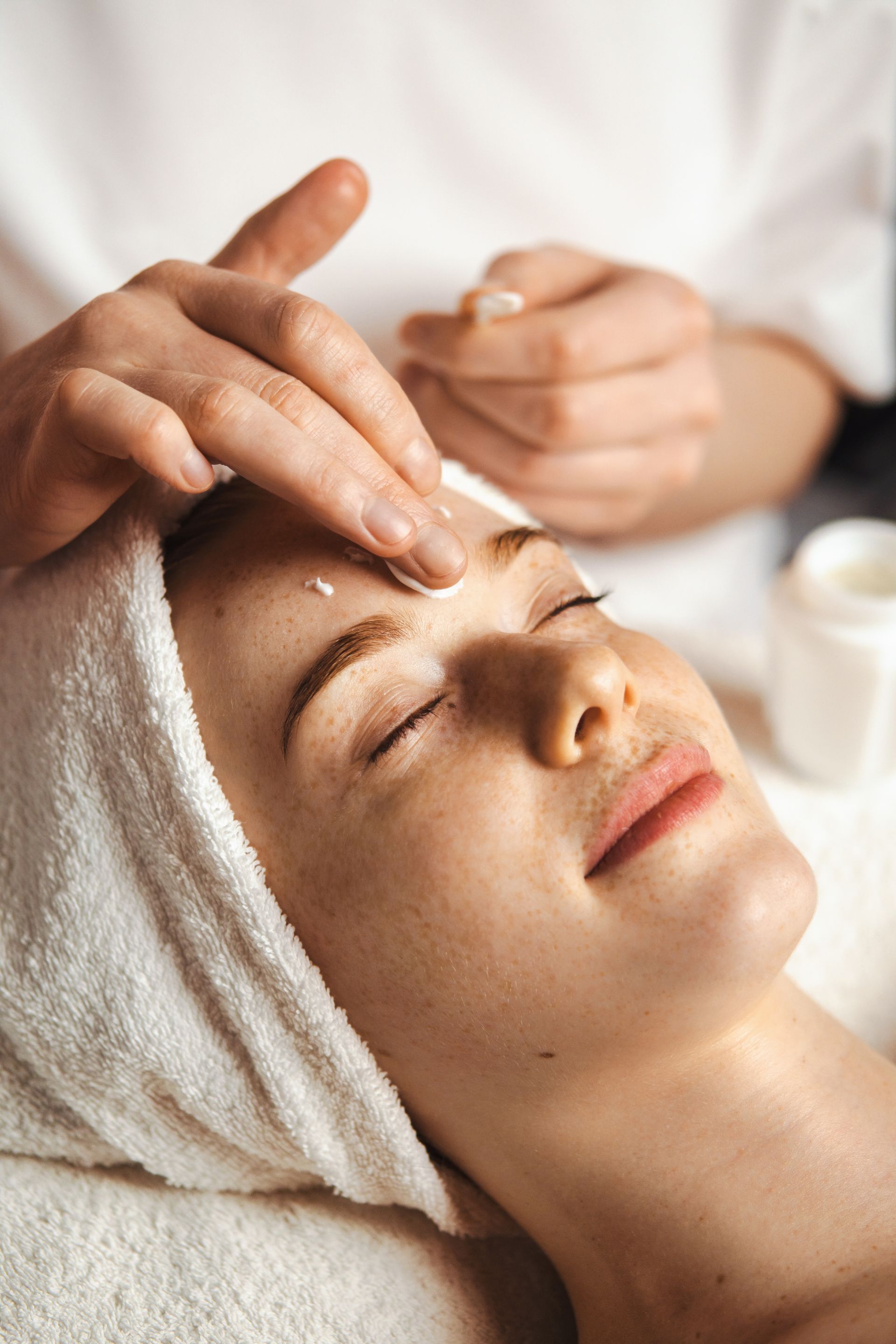 A woman with a towel wrapped around her head is getting a facial treatment at a spa.