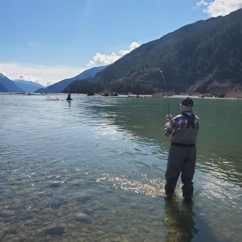 A man is fishing in a lake with mountains in the background
