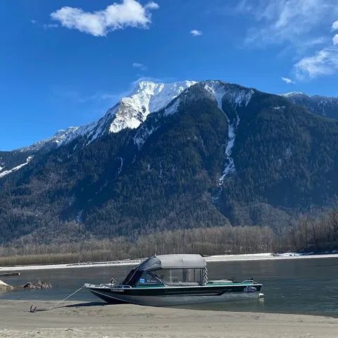 A boat is sitting on the shore of a lake with mountains in the background.