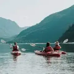 A group of people are kayaking on a lake with mountains in the background.
