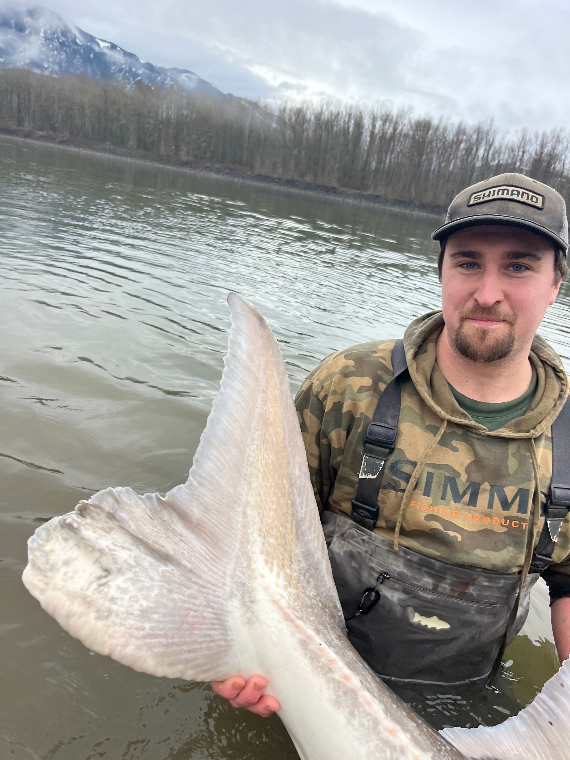 man holding sturgeon tail in river