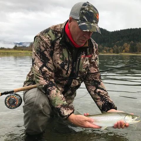 A man is kneeling in the water holding a fish.