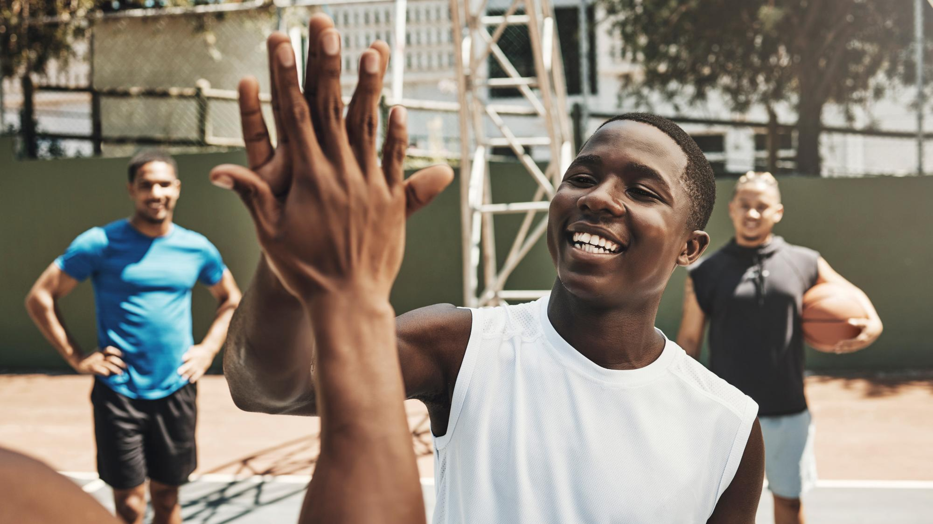 Uma pessoa vestindo uma regata branca sorri enquanto cumprimenta com um 