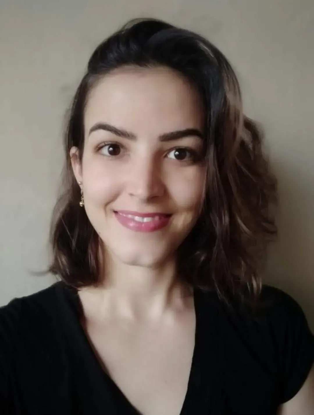 Mulher de cabelos castanhos e camisa preta sorri para a câmera.