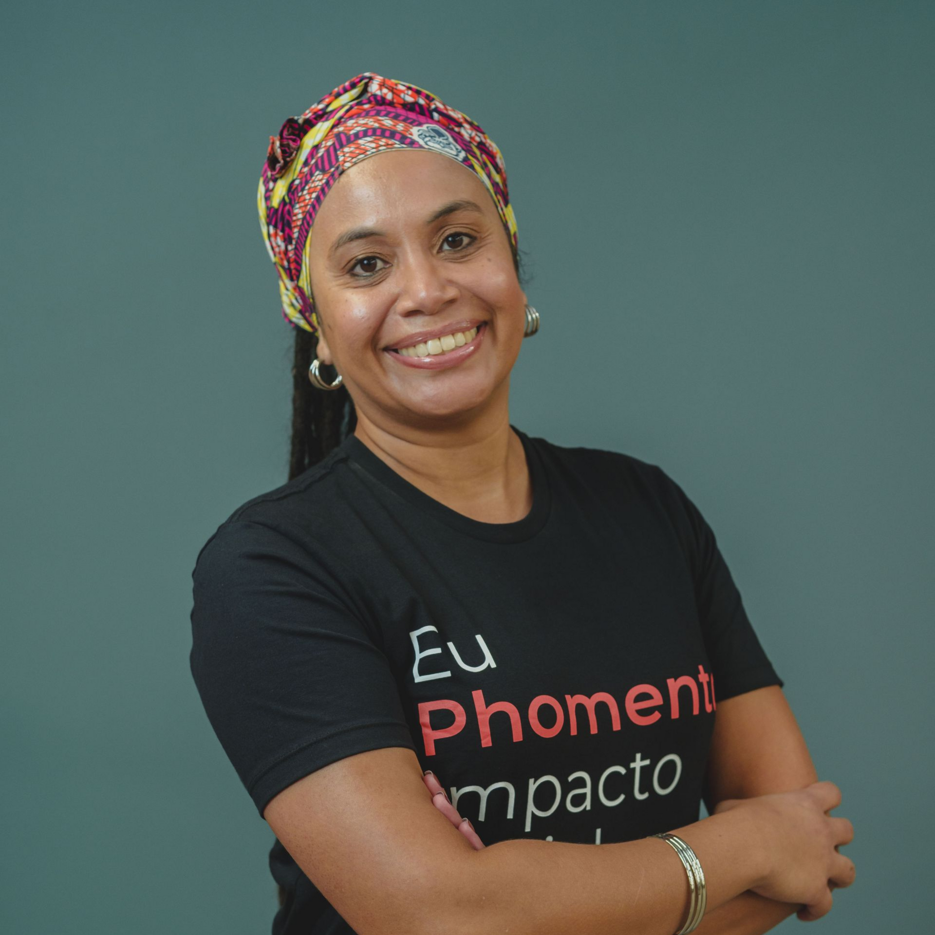 Mulher com dreadlocks e lenço laranja na cabeça, vestindo uma camisa branca com os dizeres 