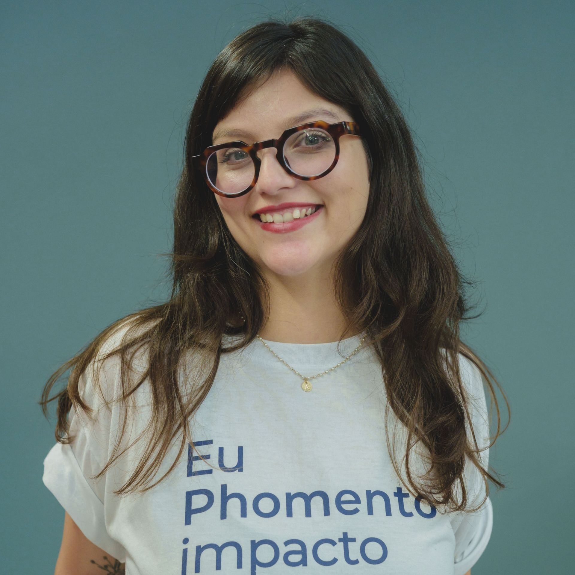 Mulher com cabelos com mechas rosa, óculos, camisa branca com os dizeres 