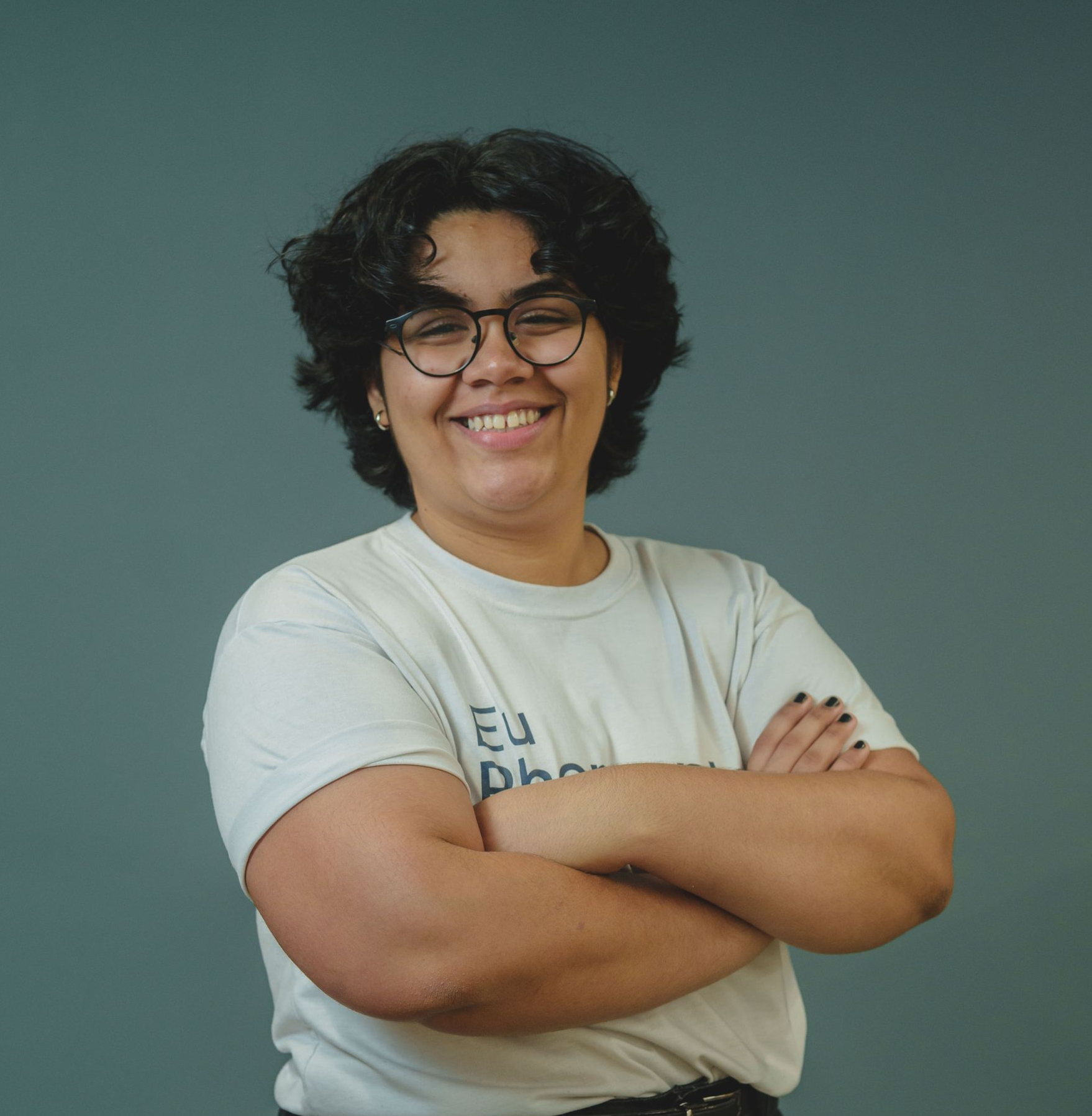 Pessoa com cabelo escuro e cacheado e óculos sorrindo para a câmera.