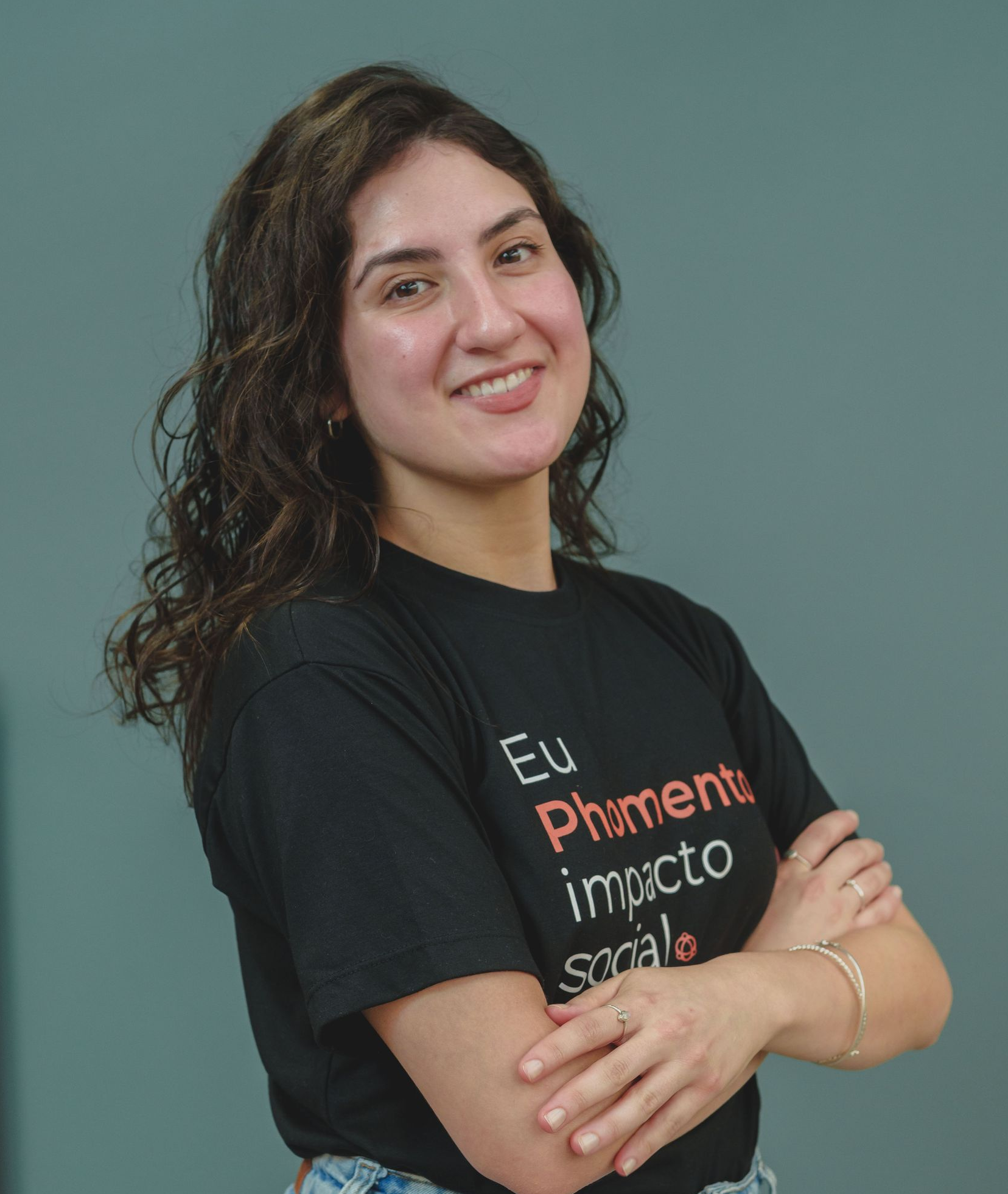 Mulher com cabelos escuros sorrindo, vestindo uma blusa preta, contra um fundo cinza claro.