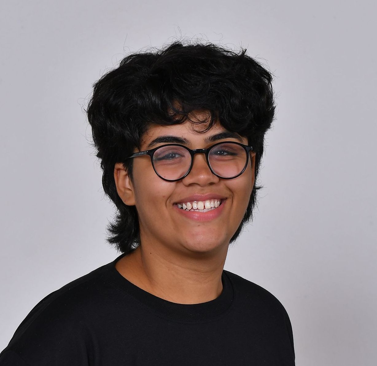 Pessoa com cabelo escuro e cacheado e óculos sorrindo para a câmera.