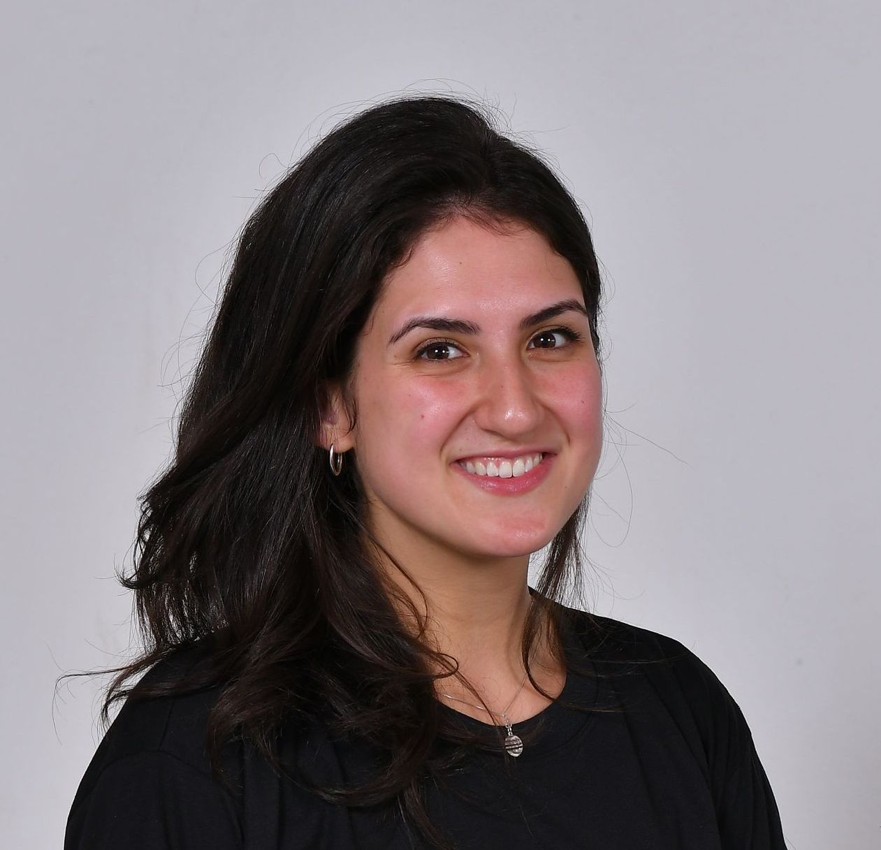 Mulher com cabelos escuros sorrindo, vestindo uma blusa preta, contra um fundo cinza claro.