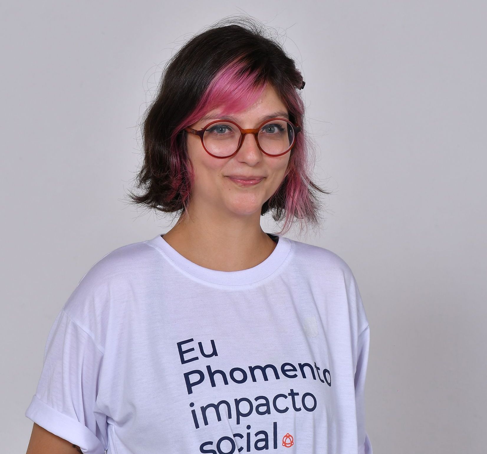 Mulher com cabelos com mechas rosa, óculos, camisa branca com os dizeres 