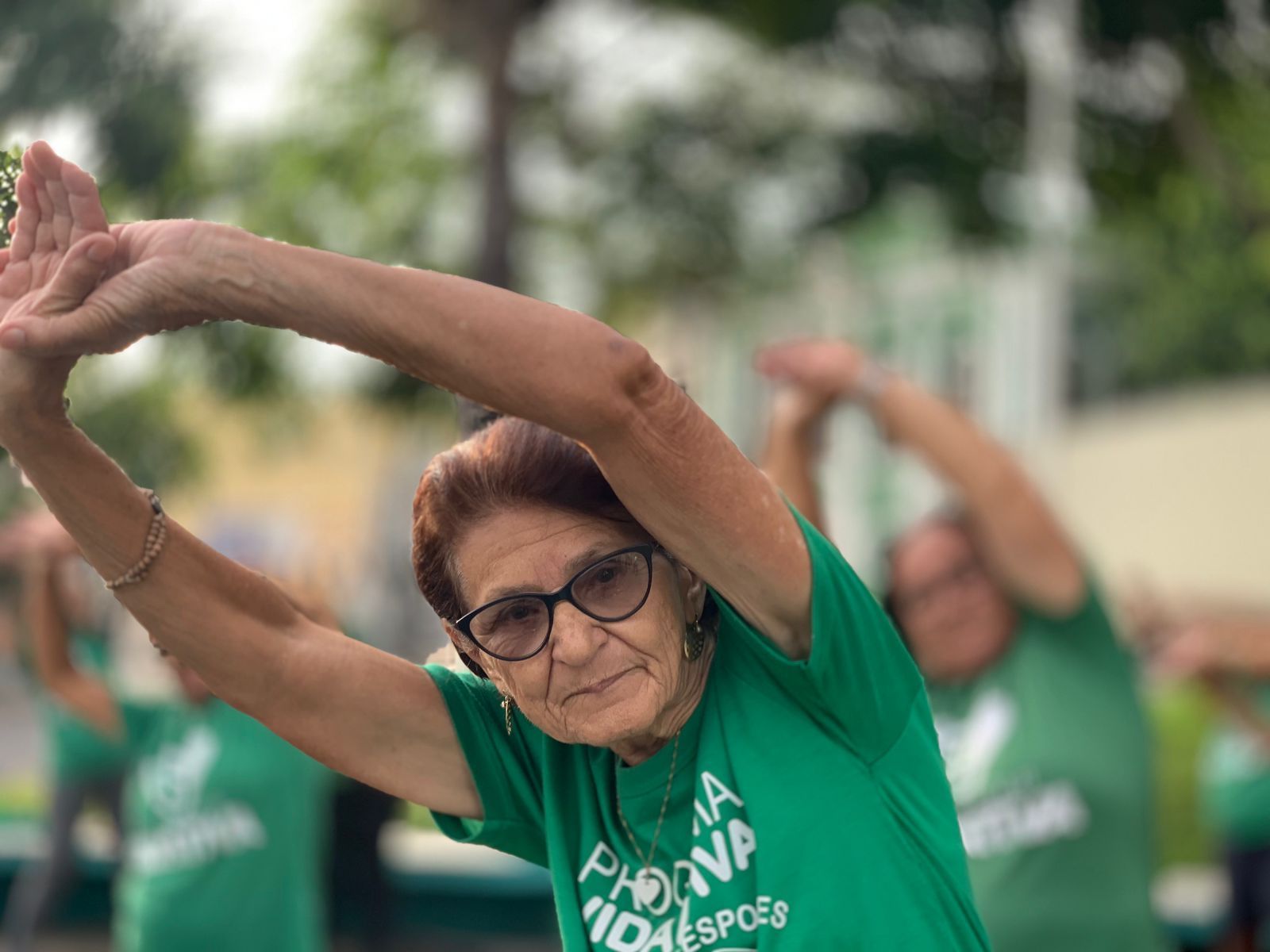 A woman in a green shirt is stretching her arms.