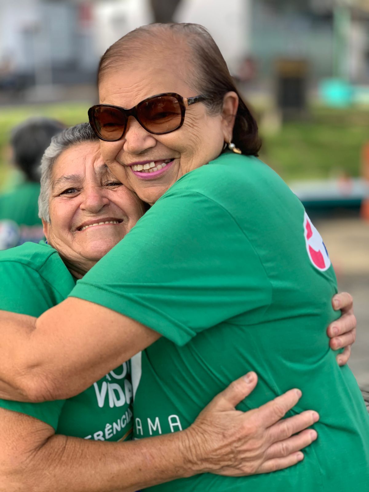 Mulheres idosas, com camisas verdes, em um abraço