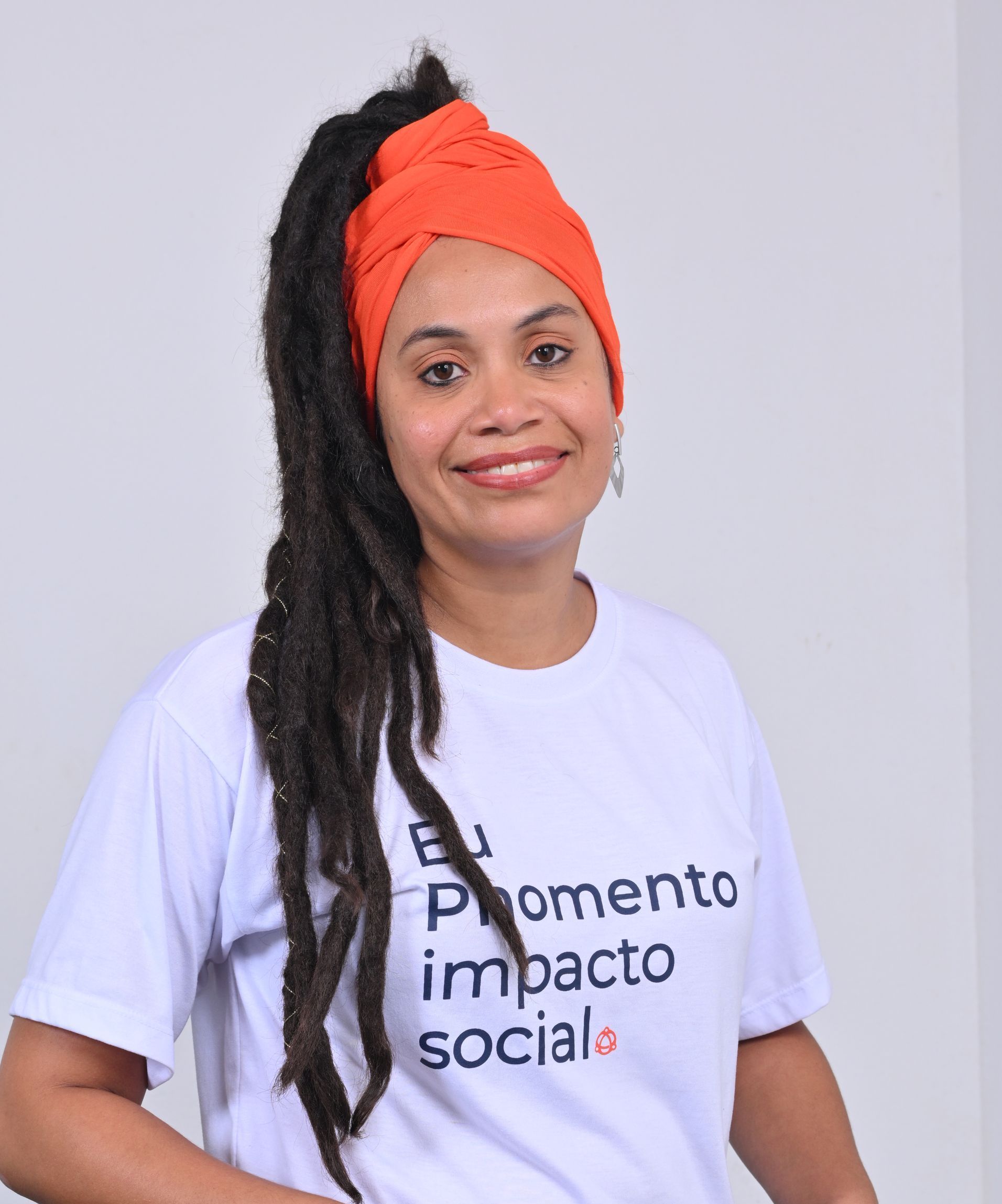 Mulher com dreadlocks e lenço laranja na cabeça, vestindo uma camisa branca com os dizeres 
