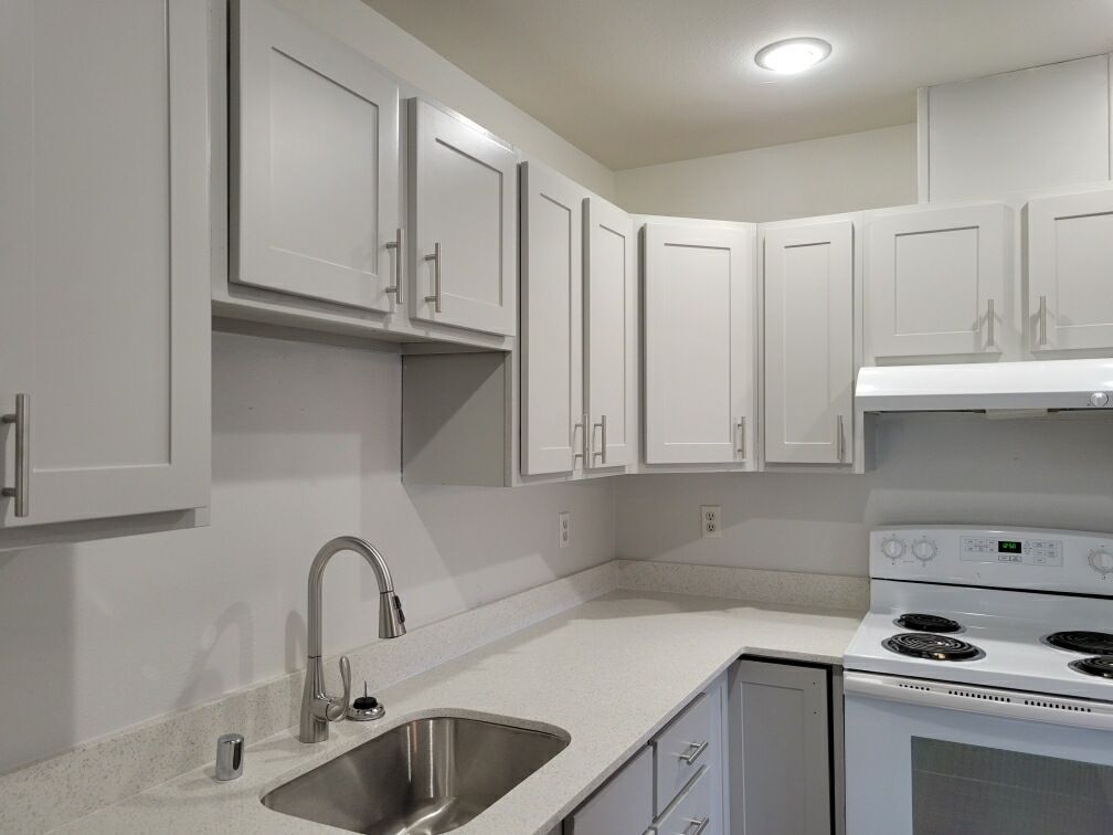 A kitchen with white cabinets , a sink , and a stove.