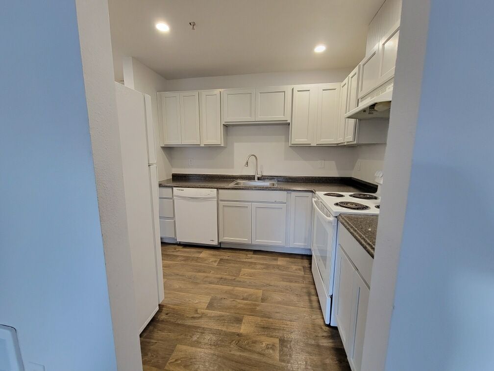A kitchen with white cabinets , a stove , a refrigerator , and a sink.
