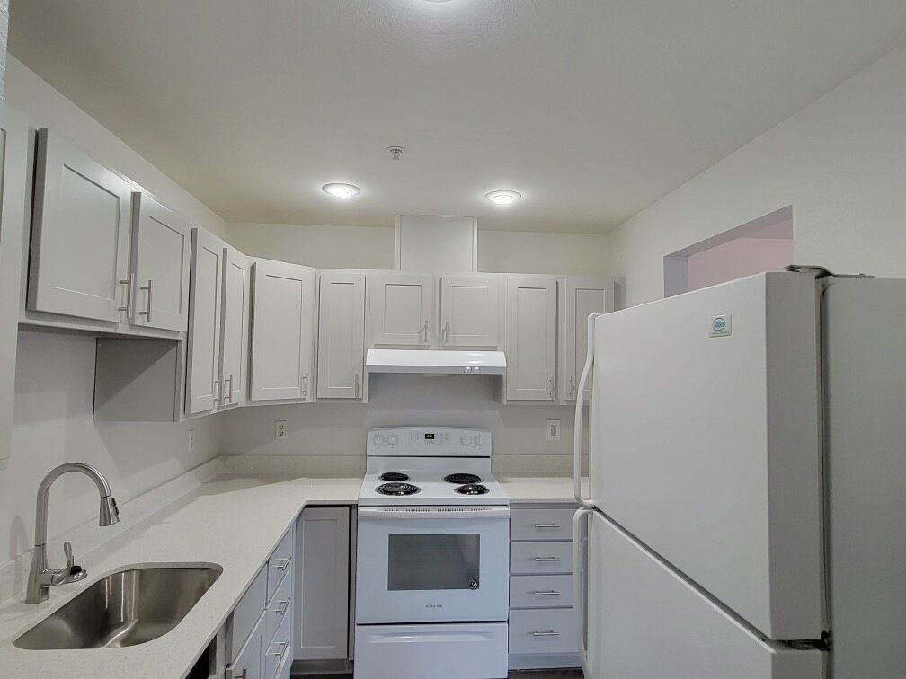 A kitchen with white cabinets , a stove , a refrigerator , and a sink.
