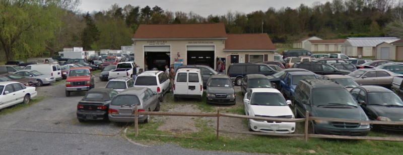 An auto repair shop with multiple vehicles in front. Brown building with two garage bays and a car lot.