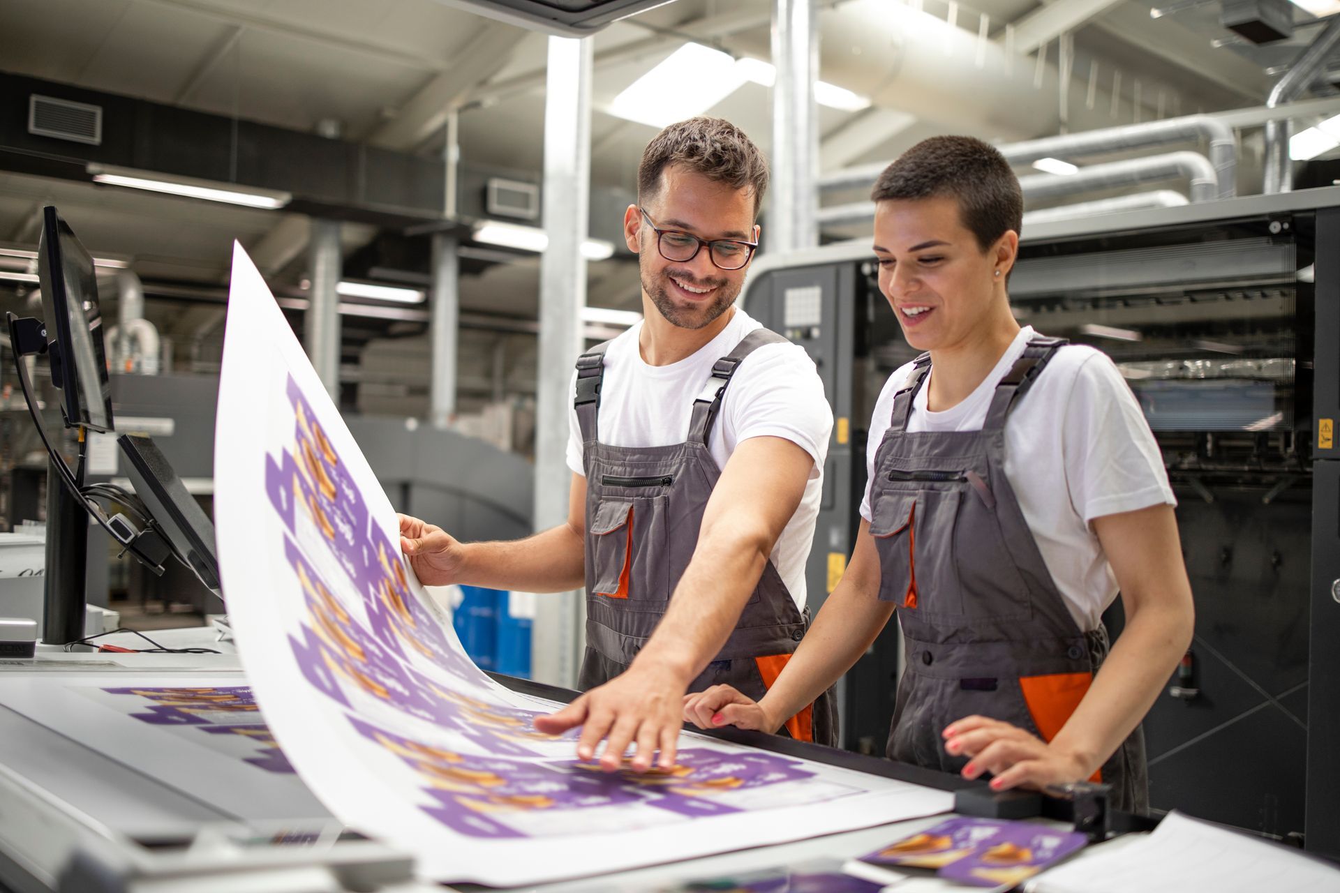 Two workers in gray overalls are checking the imprint quality at a commercial printer. Two workers in gray overalls are checking the imprint quality at a commercial printer.