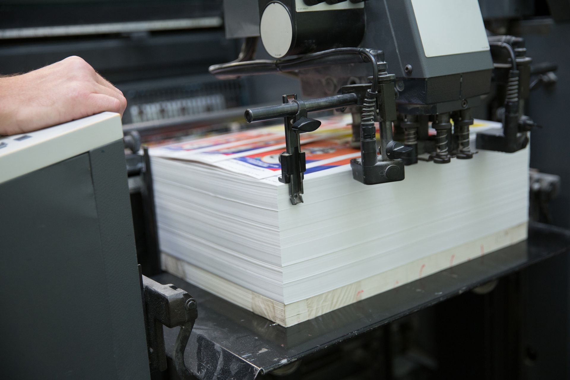 Digital printer processes stack of papers as operator monitors machine's rollers and clamps.
