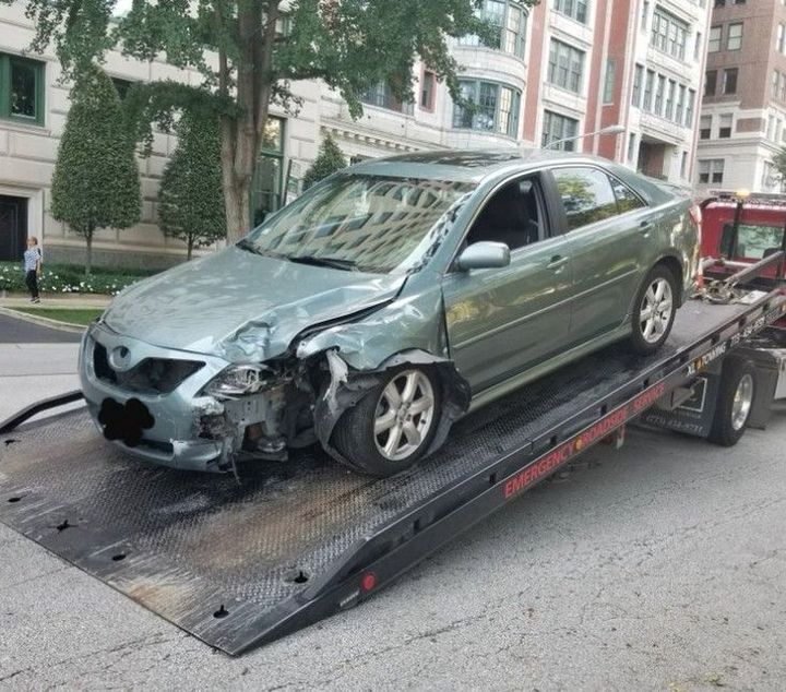 Silver car being towed on a flatbed tow truck, secured with straps.