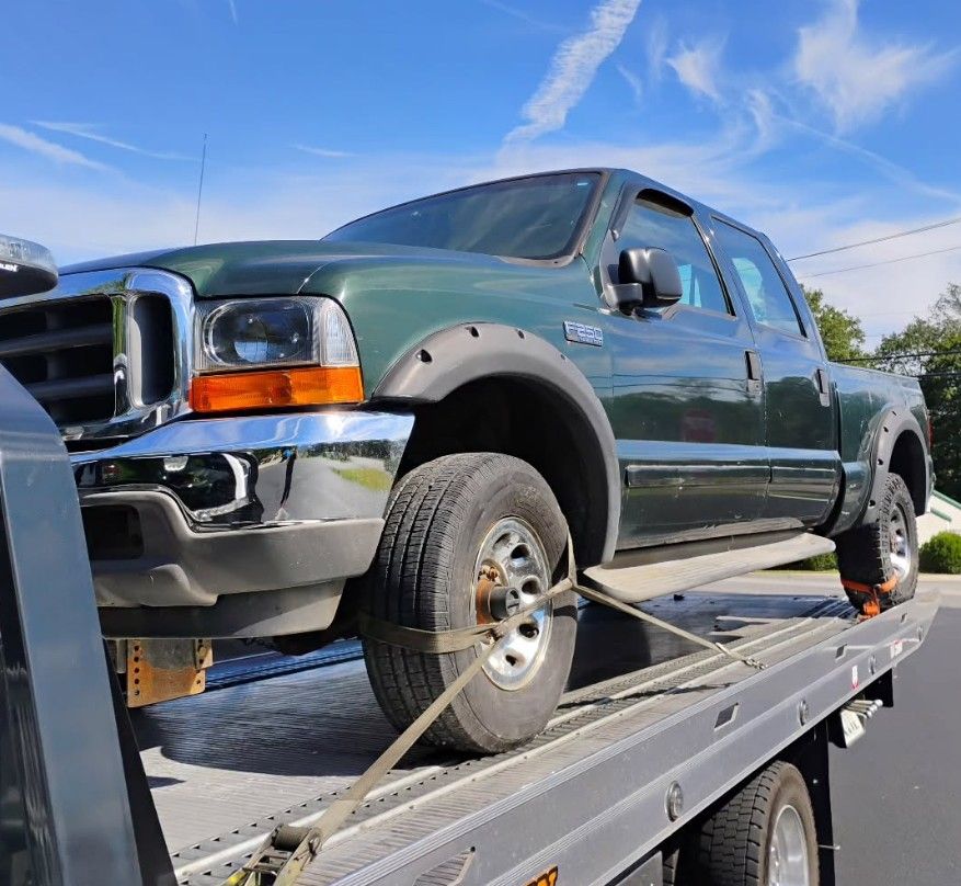Tow truck carrying a black car on a road next to a building.