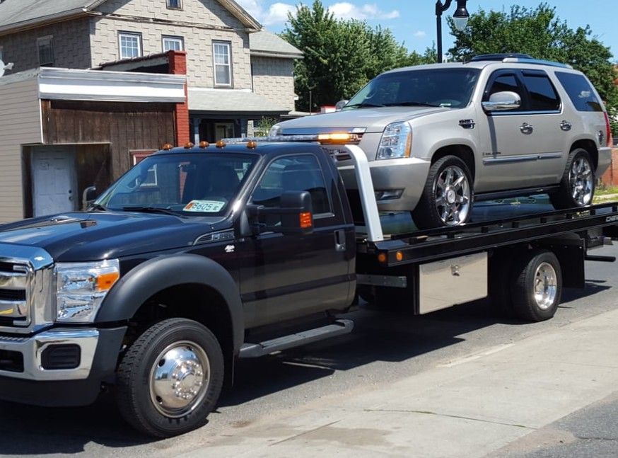 Silver car on a black tow truck bed, ready for transport.