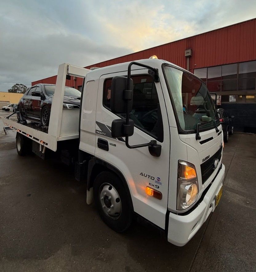 Black car being towed by a white tow truck, both on pavement.