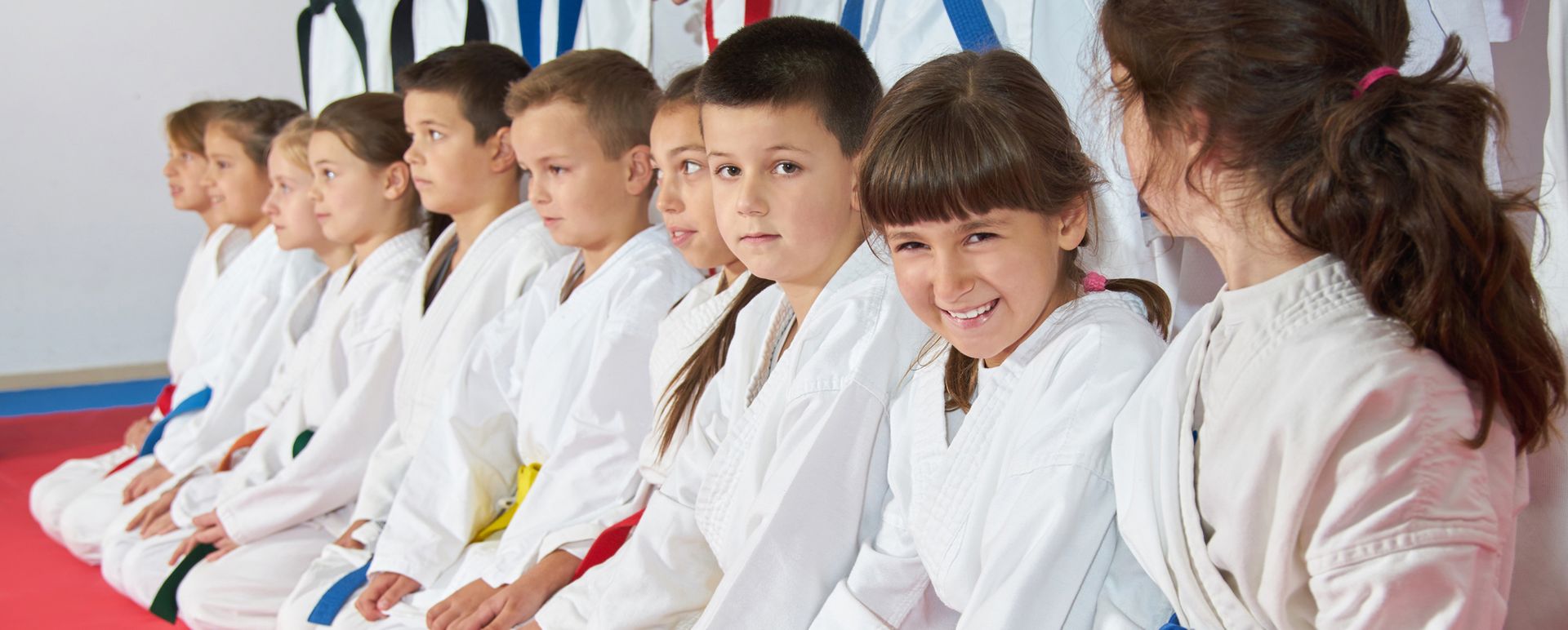 A group of children in karate uniforms are sitting in a row.