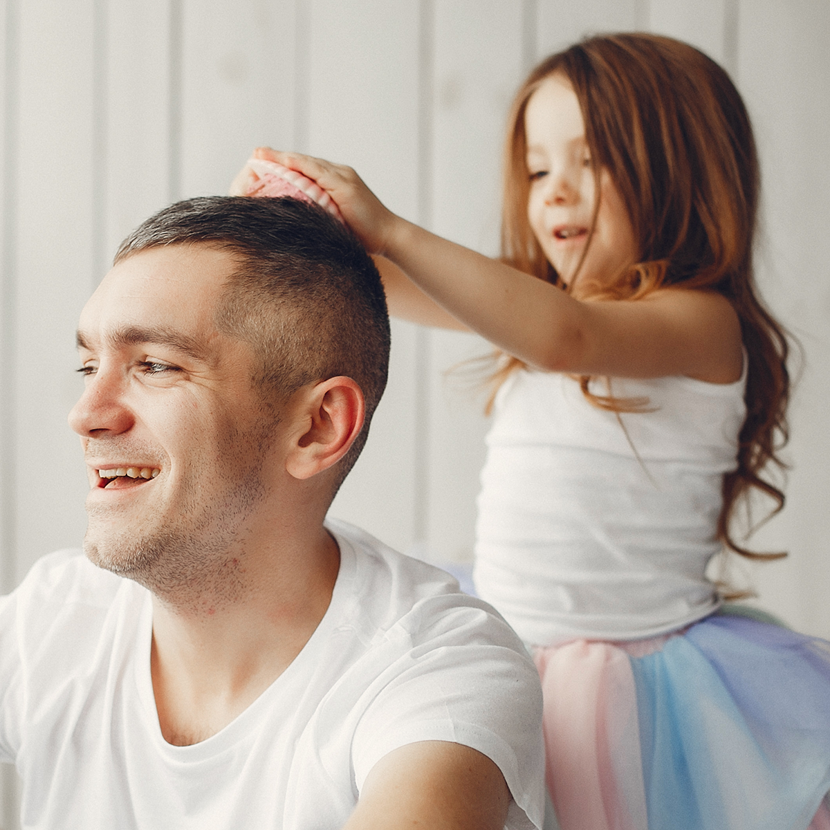 A little girl is putting a ponytail on a man 's head.