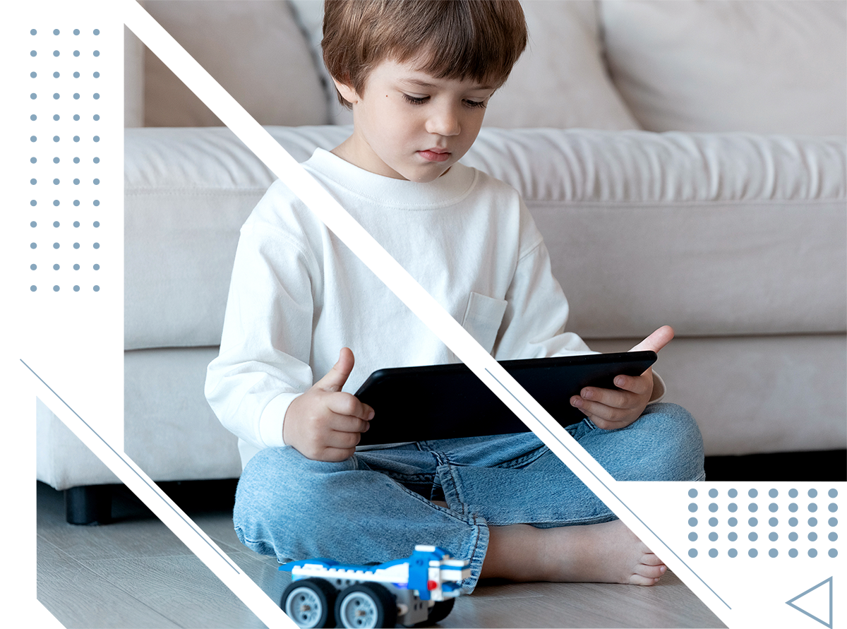 A young boy is sitting on the floor playing with a toy truck and a tablet.