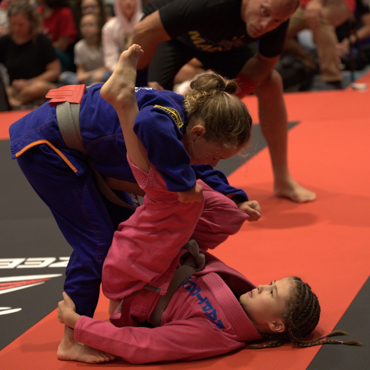 A girl in a pink jiu jitsu uniform is laying on the ground