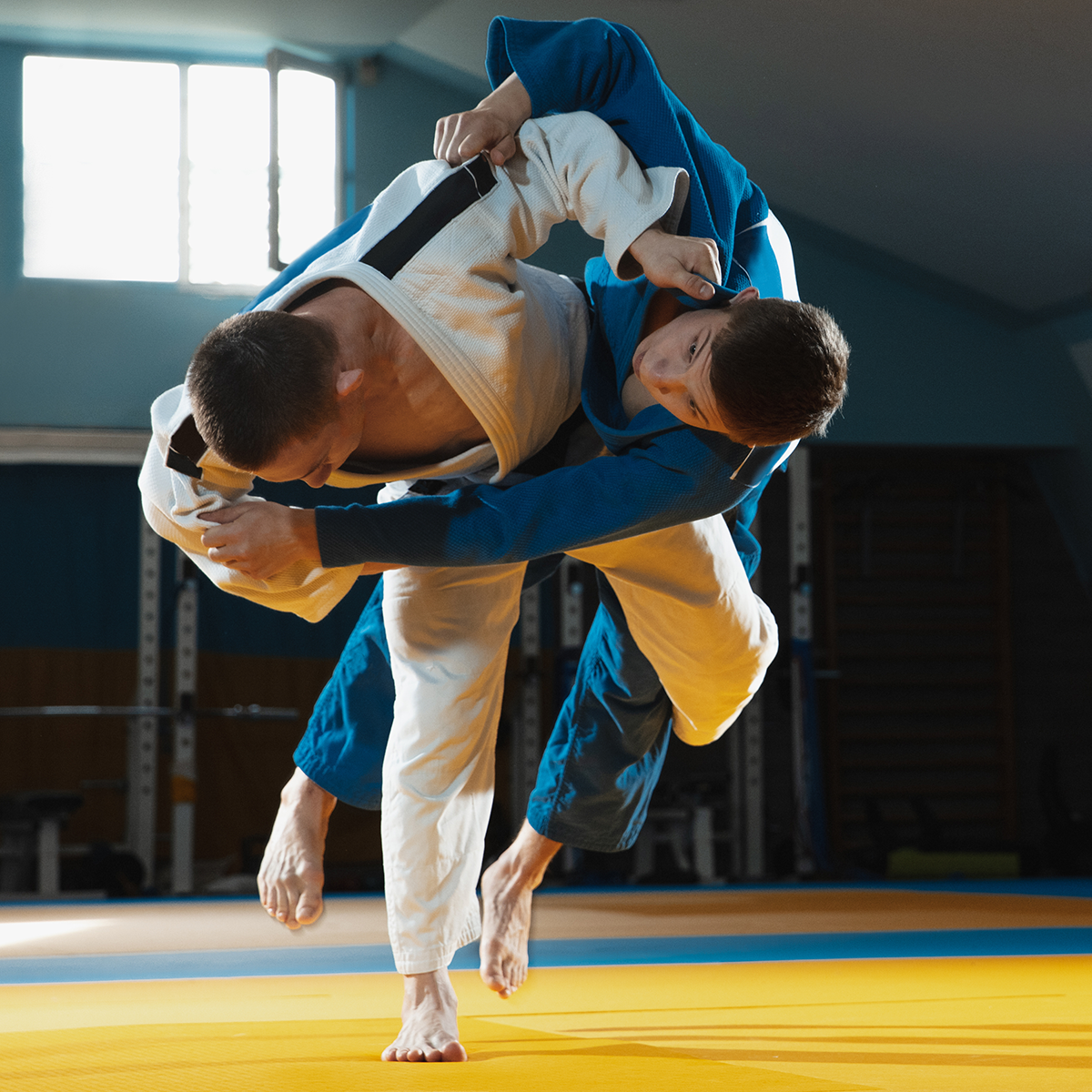 Two men are practicing judo on a mat in a gym.