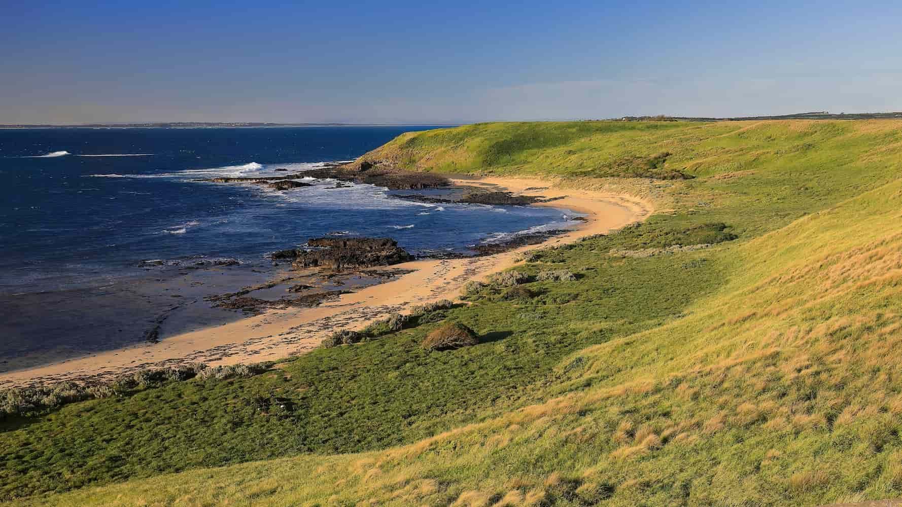 A Beach With a Grassy Hill and a Body of Water in the Background — JNQ Solar & Electrical in Fairy Meadow, NSW