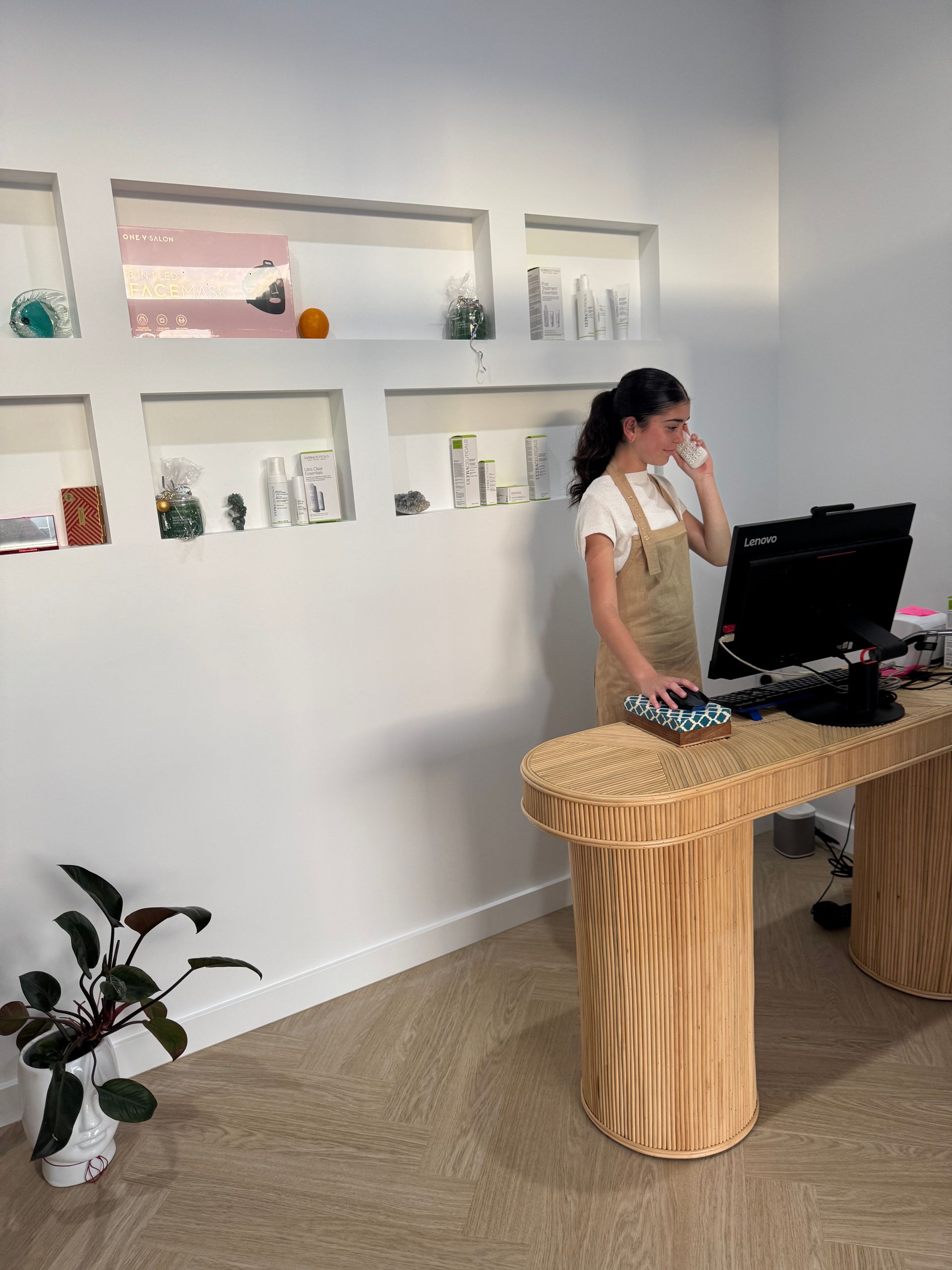 Woman in overalls on phone at wooden desk in bright office, built-in wall shelves  — Aqua Marine Skin and Beauty in Tuncurry, NSW