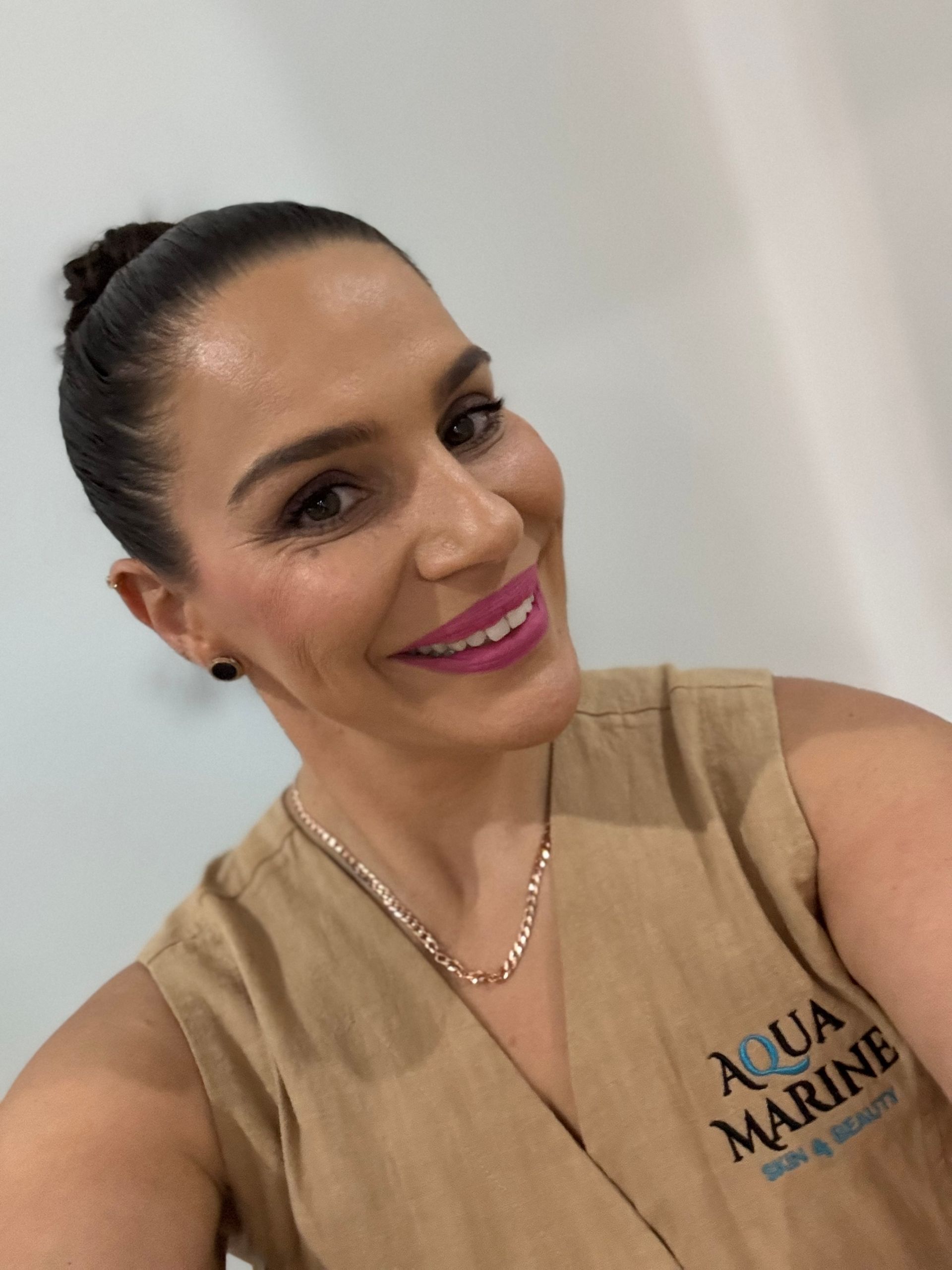 Woman in tan uniform smiles, wearing a necklace. The uniform has 