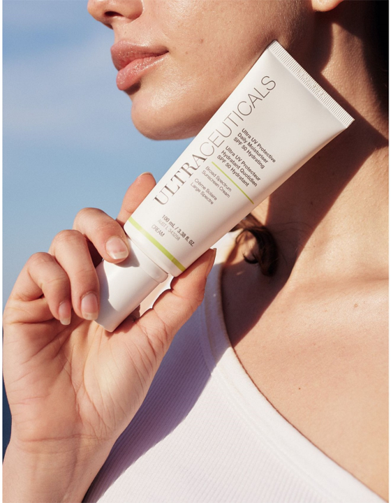 Woman holding a white Ultraceuticals skincare tube, near her neck, outdoors. — Aqua Marine Skin and Beauty in Tuncurry, NSW
