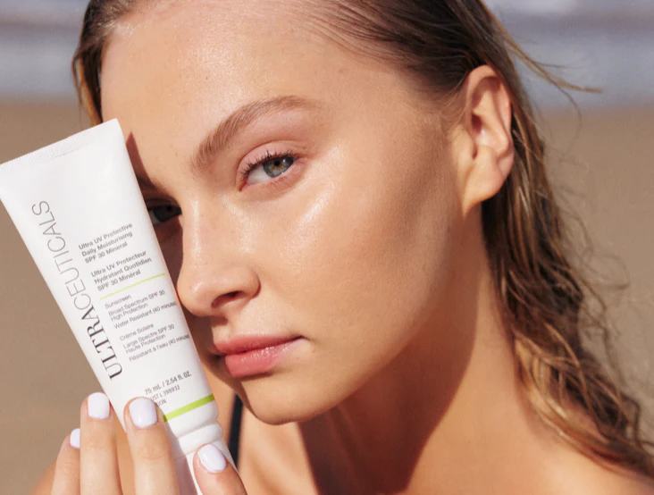 Woman with fair skin holding Ultraceuticals sunscreen on a beach, looking at camera. — Aqua Marine Skin and Beauty in Tuncurry, NSW