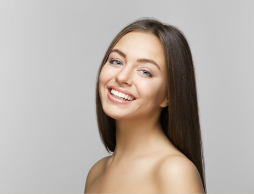 Woman with long brown hair smiles, looking at the camera, neutral gray background. — Aqua Marine Skin and Beauty in Tuncurry, NSW