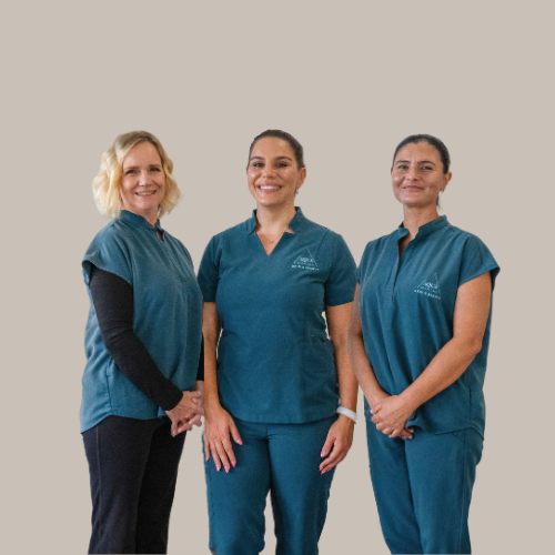 Three women in teal scrubs smiling, standing in a neutral-coloured room. — Aqua Marine Skin and Beauty in Tuncurry, NSW