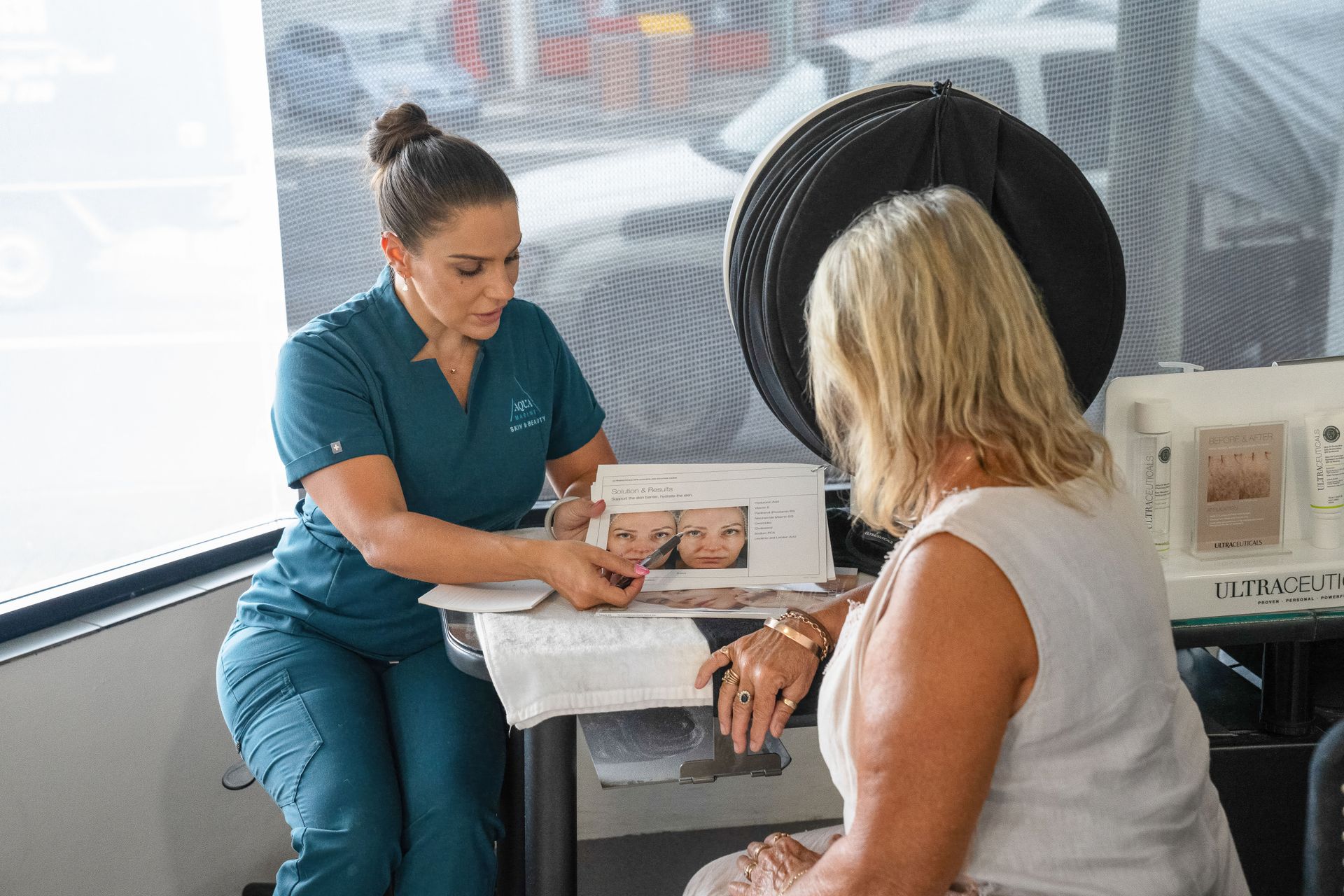 A medical professional shows a patient before/after photos of a skin treatment in an office. — Aqua Marine Skin and Beauty in Tuncurry, NSW